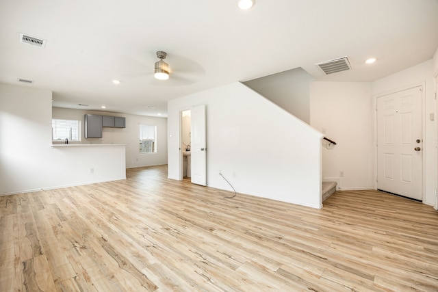 unfurnished living room featuring ceiling fan, light wood finished floors, stairs, and visible vents