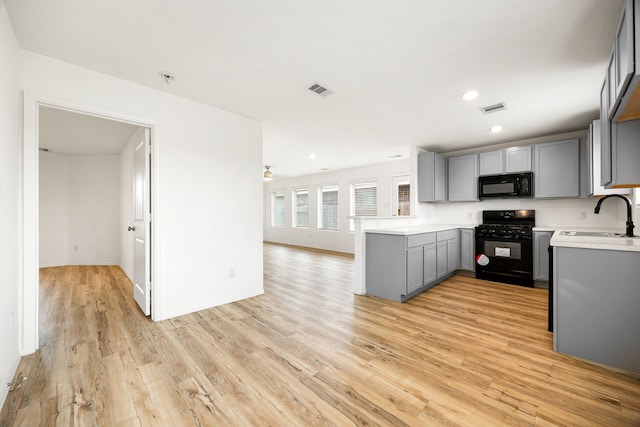 kitchen featuring light wood finished floors, a sink, visible vents, gray cabinets, and black appliances