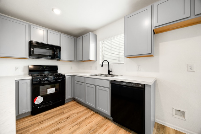 kitchen with light countertops, a sink, gray cabinetry, light wood-style flooring, and black appliances
