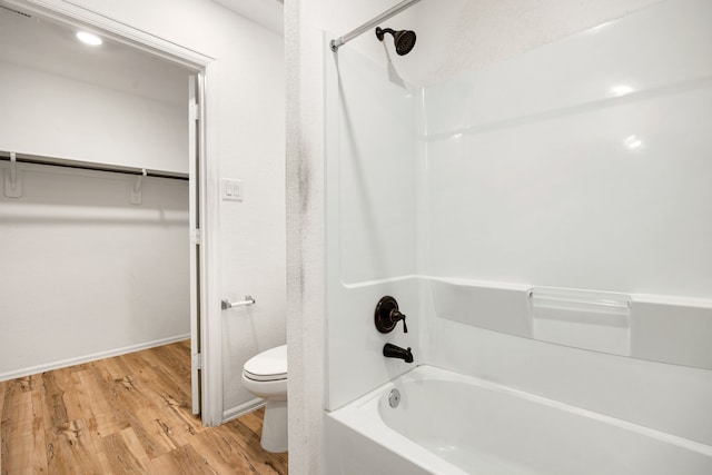 bathroom featuring bathtub / shower combination, wood finished floors, a walk in closet, and toilet