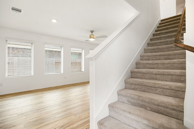staircase featuring wood finished floors, visible vents, a ceiling fan, and baseboards