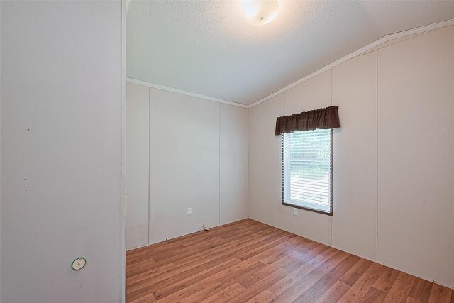 unfurnished room featuring light wood-style floors, vaulted ceiling, a textured ceiling, and ornamental molding