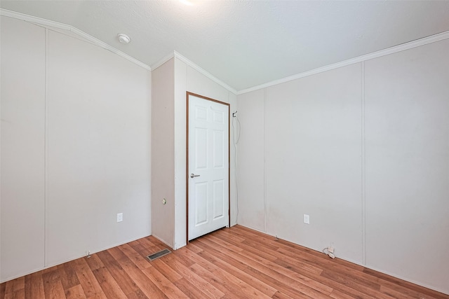 unfurnished room with vaulted ceiling, crown molding, light wood finished floors, and visible vents