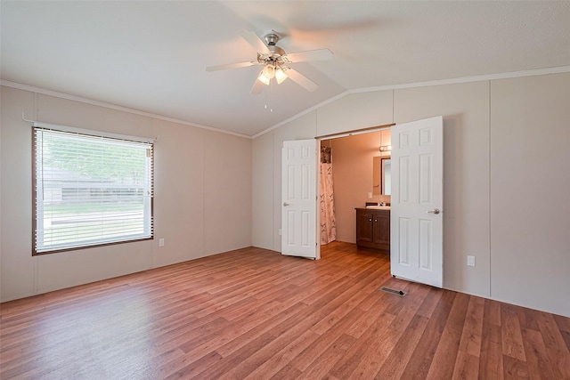 unfurnished bedroom featuring vaulted ceiling, light wood-style floors, ensuite bath, crown molding, and ceiling fan