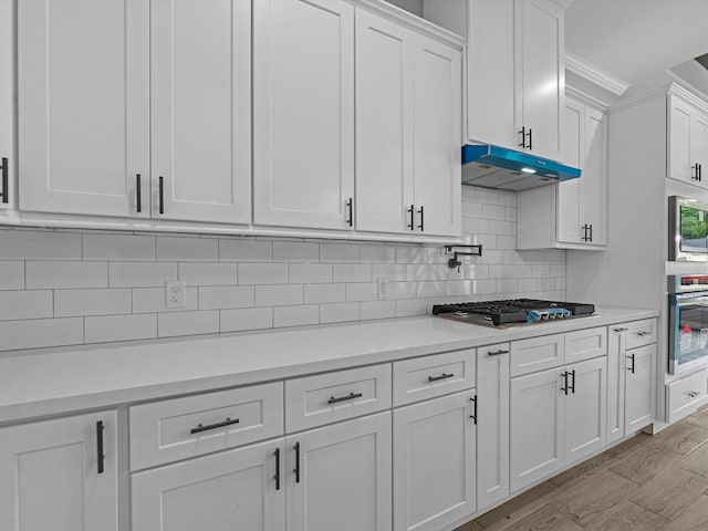 549 Rd 660, Dayton, TX 77535 - kitchen with white cabinets, stainless steel appliances, tasteful backsplash, light countertops, and under cabinet range hood
