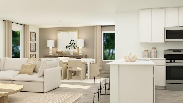 kitchen featuring open floor plan, stainless steel range with electric stovetop, light wood-type flooring, white microwave, and white cabinets