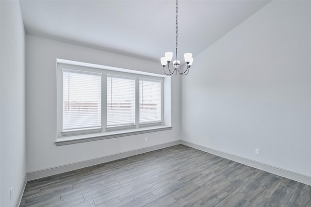 unfurnished room featuring baseboards, wood finished floors, and a chandelier