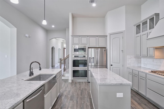 kitchen featuring stainless steel appliances, dark wood-style floors, arched walkways, light stone counters, and a kitchen island