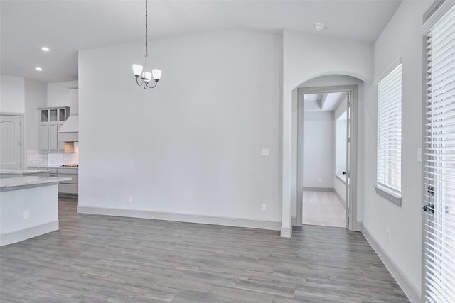 unfurnished dining area featuring arched walkways, a chandelier, wood finished floors, and recessed lighting