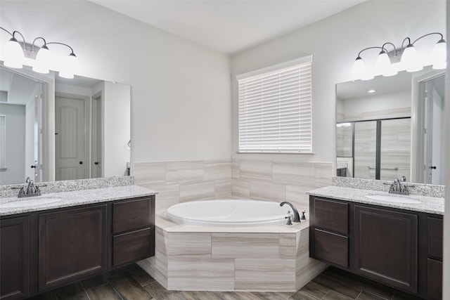 bathroom with two vanities, a bath, a stall shower, and a sink