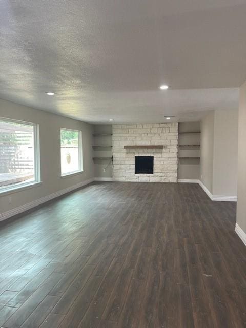 unfurnished living room with a textured ceiling, baseboards, built in features, and dark wood-type flooring