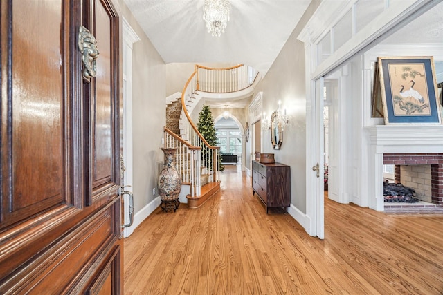 entryway featuring stairway, light wood-style floors, an inviting chandelier, a fireplace, and baseboards