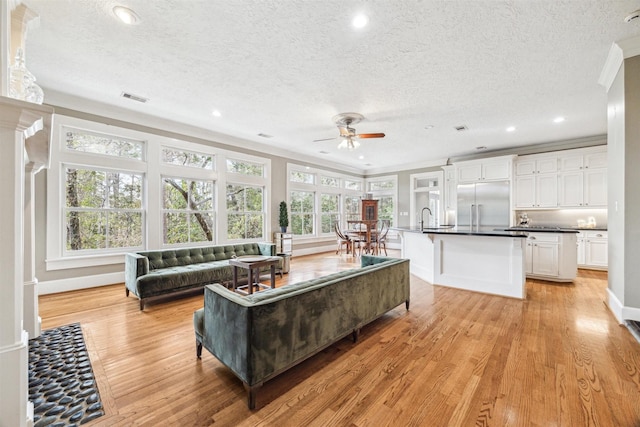 living area with light wood finished floors, a textured ceiling, recessed lighting, ceiling fan, and crown molding