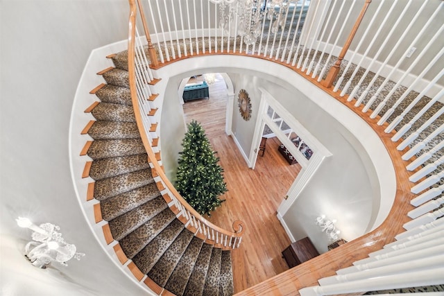 staircase with an inviting chandelier, wood finished floors, a high ceiling, and arched walkways