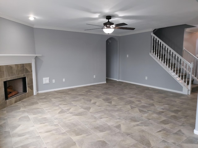 unfurnished living room featuring a tile fireplace, ornamental molding, arched walkways, stairs, and ceiling fan