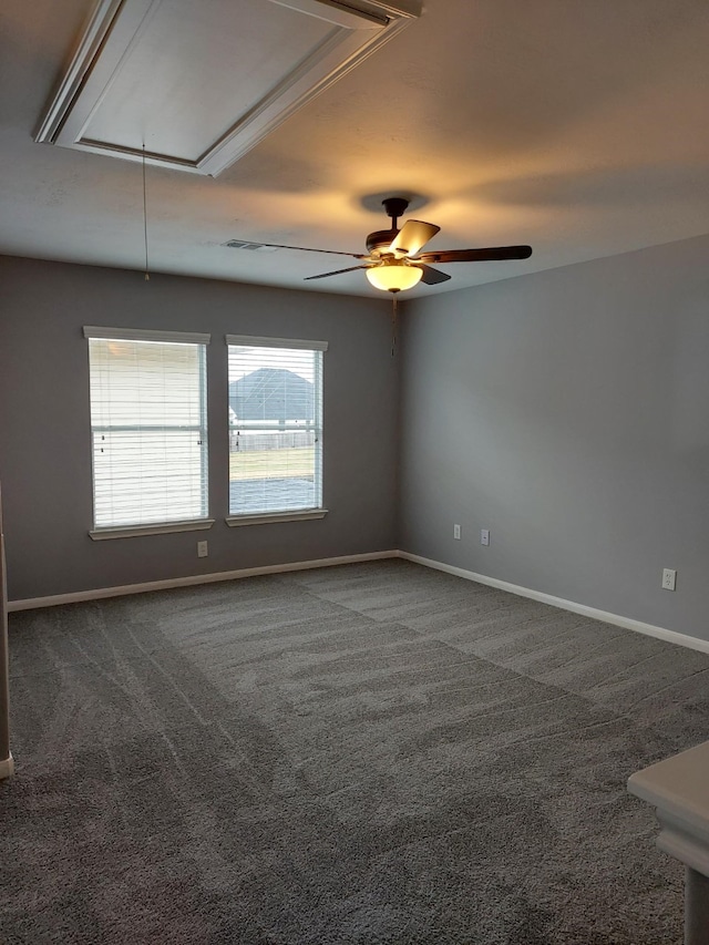 unfurnished room featuring attic access, dark colored carpet, baseboards, and ceiling fan
