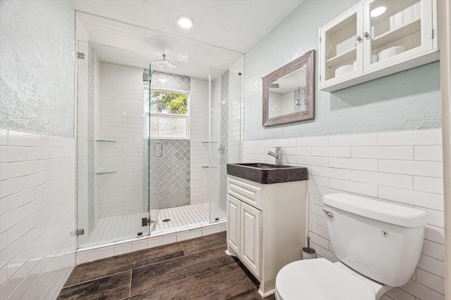 full bathroom featuring wood finished floors, a stall shower, vanity, tile walls, and toilet