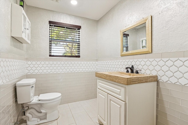 bathroom with tile patterned flooring, tile walls, toilet, and a wainscoted wall