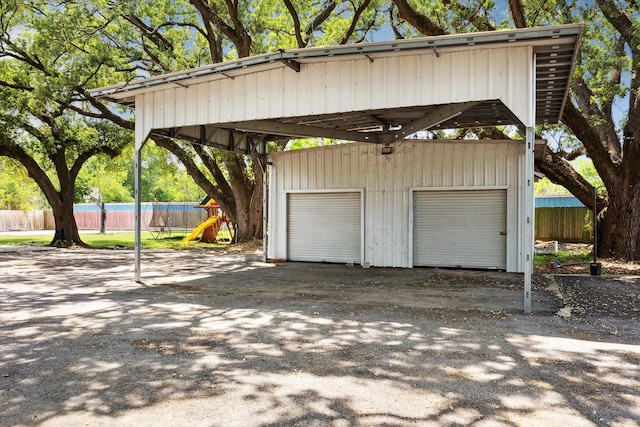 detached garage featuring fence and a carport