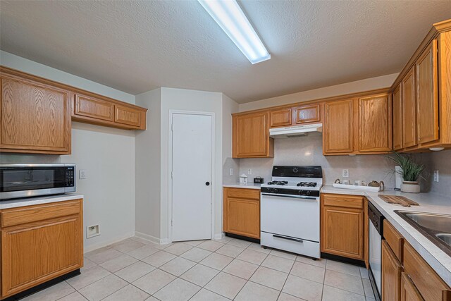 215 Pebble Canyon Ln, Dickinson, TX 77539 - kitchen featuring appliances with stainless steel finishes, under cabinet range hood, light countertops, a textured ceiling, and light tile patterned floors