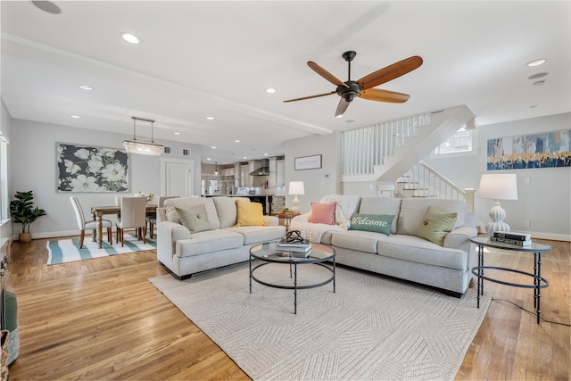 living room with a ceiling fan, baseboards, stairway, and light wood-style floors