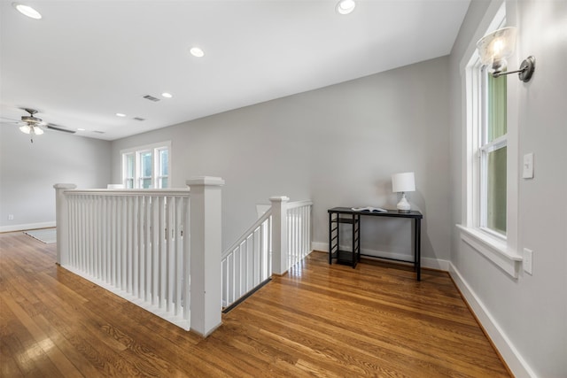 corridor with baseboards, recessed lighting, wood finished floors, and an upstairs landing