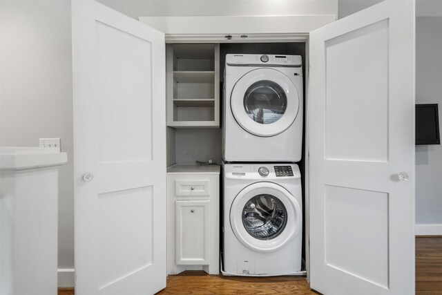 laundry room featuring wood finished floors, cabinet space, and stacked washer / drying machine