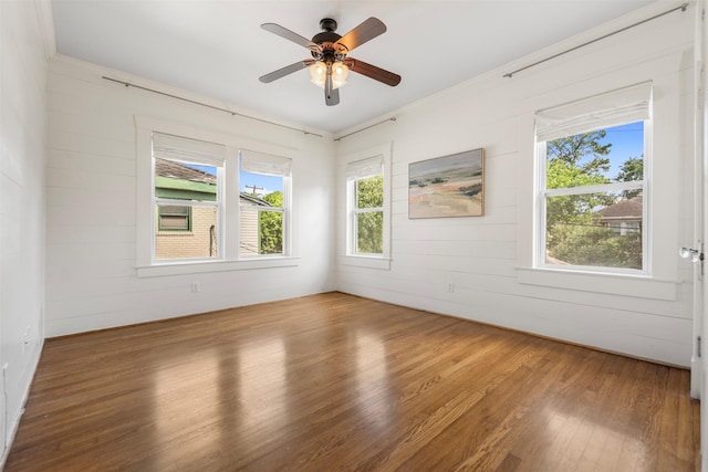 spare room featuring wooden walls, a ceiling fan, and wood finished floors