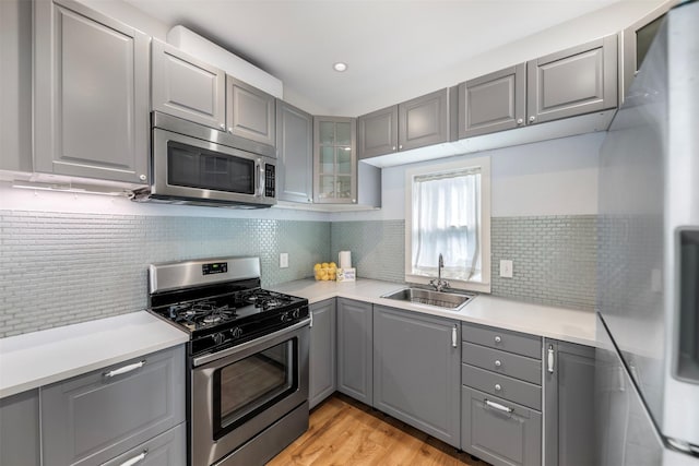 kitchen with light wood-type flooring, light countertops, a sink, gray cabinetry, and stainless steel appliances