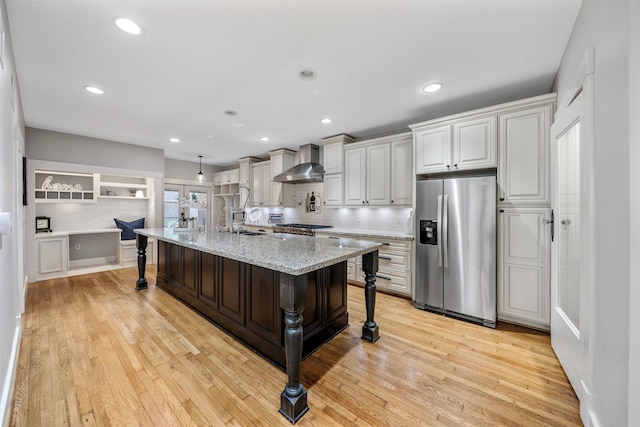 kitchen featuring stainless steel fridge, a kitchen breakfast bar, light wood-type flooring, and wall chimney exhaust hood