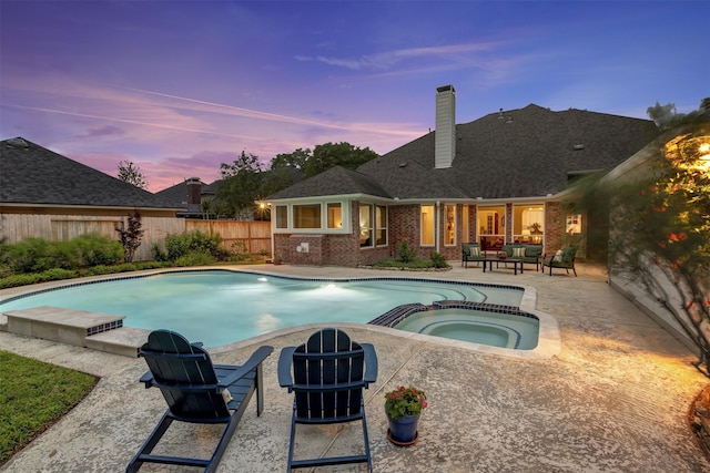 pool at dusk featuring a patio, fence, and a pool with connected hot tub