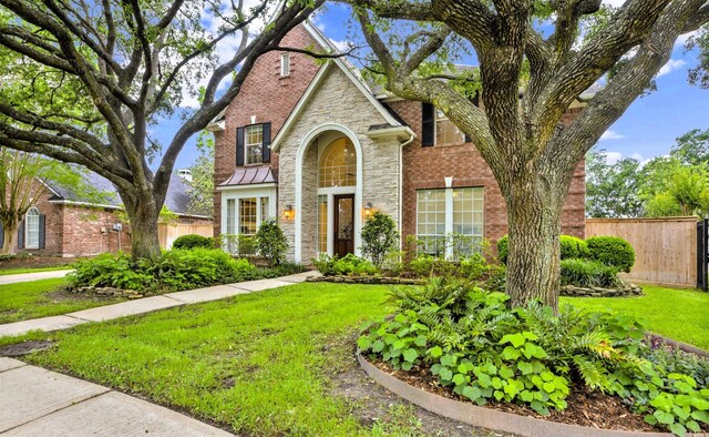 view of front of home with fence, a front yard, brick siding, and stone siding