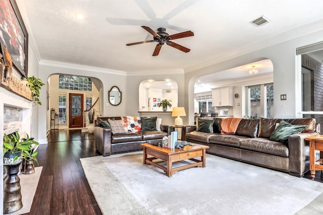 living area featuring ceiling fan, dark wood-style flooring, visible vents, crown molding, and arched walkways