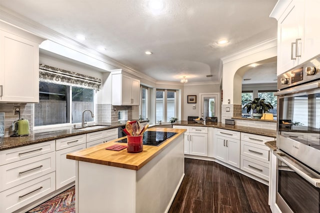 kitchen with ornamental molding, stainless steel double oven, black electric cooktop, a sink, and wood counters