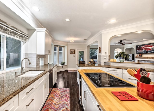kitchen featuring butcher block counters, black electric stovetop, arched walkways, a sink, and backsplash