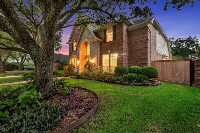 view of front of home with fence, a lawn, and brick siding