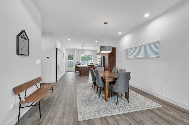 dining space with recessed lighting, a barn door, light wood-style floors, and baseboards
