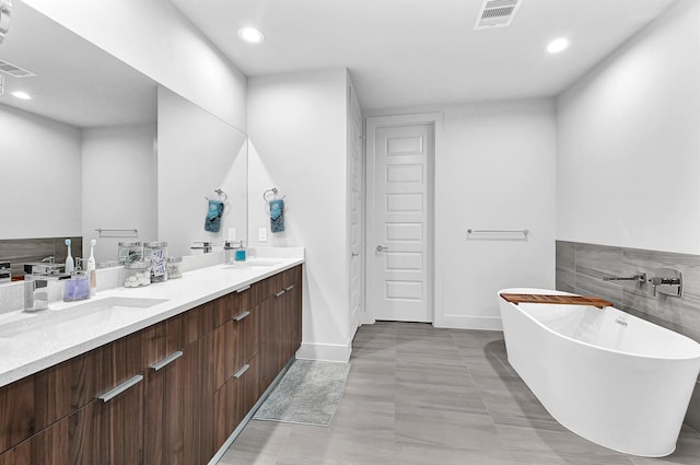 bathroom featuring double vanity, visible vents, a sink, and a freestanding bath