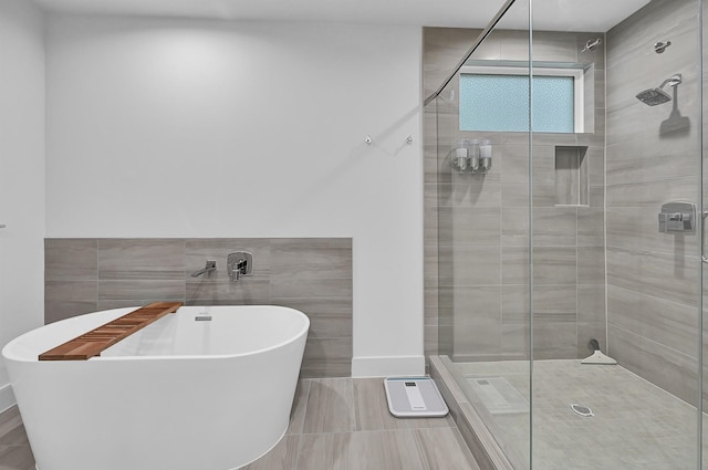 full bath with a freestanding tub, tile walls, baseboards, tile patterned floors, and a stall shower
