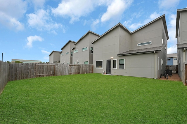 rear view of house with a lawn, stucco siding, and a fenced backyard