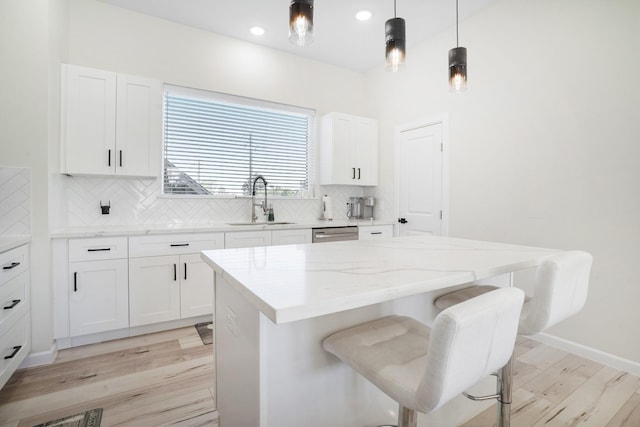 kitchen featuring a breakfast bar, a sink, light stone countertops, a kitchen island, and decorative backsplash