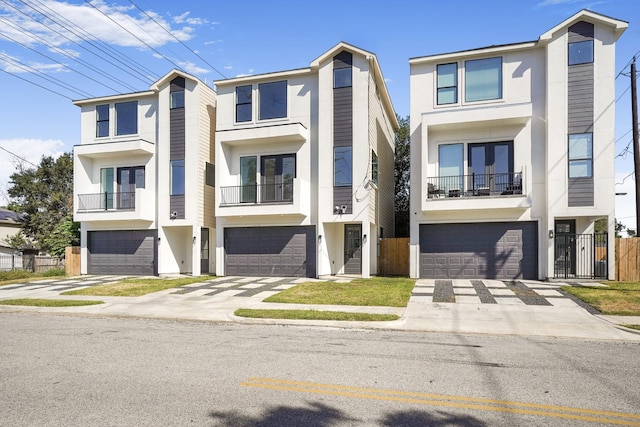 townhome / multi-family property featuring a balcony, driveway, fence, a garage, and stucco siding