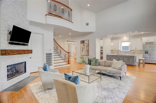 living room featuring stairway, arched walkways, a towering ceiling, light wood-style flooring, and a fireplace