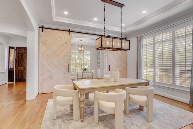 dining space featuring a tray ceiling, light wood-type flooring, crown molding, and an inviting chandelier