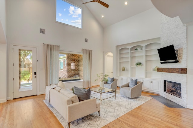 living room featuring high vaulted ceiling, a ceiling fan, a stone fireplace, light wood-style floors, and visible vents