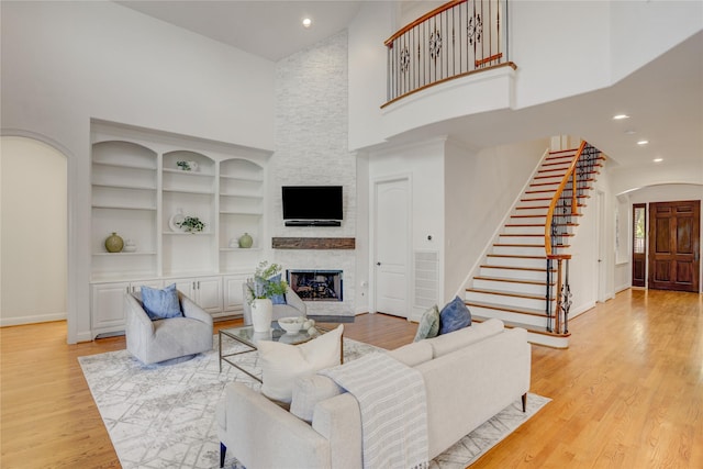 living room with stairway, arched walkways, baseboards, a fireplace, and high vaulted ceiling