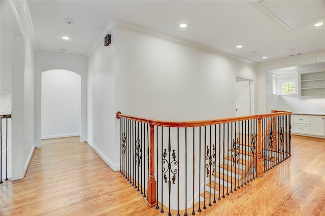 corridor with crown molding, an upstairs landing, attic access, light wood-style floors, and arched walkways