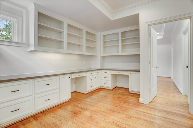 unfurnished office with built in desk, light wood finished floors, and crown molding