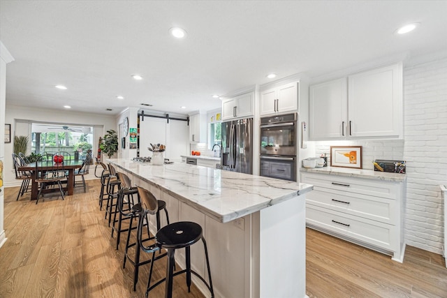 kitchen with a barn door, light wood-type flooring, a breakfast bar area, and stainless steel appliances