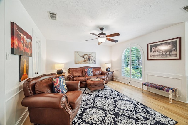 living room featuring a ceiling fan, wood finished floors, visible vents, and a textured ceiling